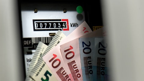 Vor einem Stromzähler sind Euro-Geldscheine zu sehen: Fünfer, Zehner und Zwanziger