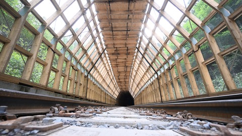 Tunnelkonstruktion aus Holz über Bahngleisen.