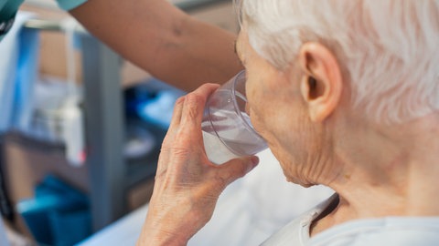 SYMBOLBILD: Eine alte Frau trinkt aus einem Glas Wasser. Vor allem bei enormer Hitze wie derzeit, aber längst nicht nur dann ist ausreichendes Trinken wichtig - doch viele Menschen in Deutschland kommen nicht auf die empfohlene Menge.