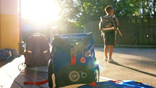 Schulranzen stehen am Morgen auf dem Schulhof einer Grundschule, die Sonne scheint hell.