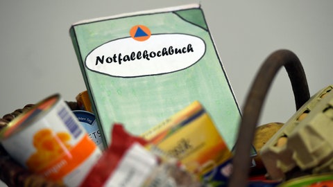 Ein Buch-Dummy liegt in einem Korb mit Lebensmitteln. Bei einem Wettbewerb um Rezeptideen für ein neues "Notfallkochbuch" sind beim Bundesamt für Bevölkerungsschutz und Katastrophenhilfe (BBK) mehr als 500 Vorschläge eingegangen.