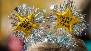 Ein Frau begrüßt das Neue Jahr mit einem Kopfschmuck mit der Aufschrift "Happy New Year".