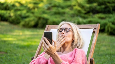 Frau wirft ihrem Smartphone einen Luftkuss zu.