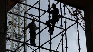 Zwei Bauarbeiter im Gegenlicht auf einem Gerüst.