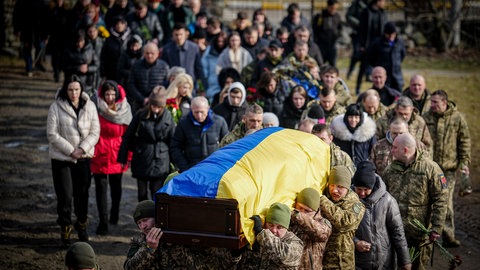 Sodaten tragen einen mit ukrainischer Flagge bedeckten Sarg, gefolgt von Trauernden