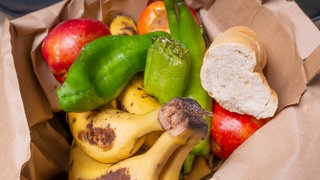 Verderbendes Obst und Brot in einem Mülleiner, Symbolbild Lebensmittelverschwendung