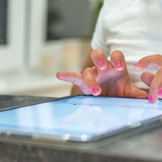 Eine Grundschülerin sitzt an einem Tabletcomputer und tippt.