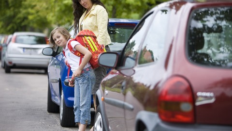 An einer Straße übt eine Mutter mit ihrer Tochter den zukünftigen Schulweg (Illustration, Archivbild)