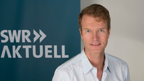 Andreas Böhnisch steht vor dem Logo von SWR Aktuell.