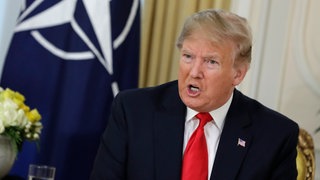 US-Präsident Donald Trump sitzt bei einer Pressekonferenz vor einer NATO-Flagge.
