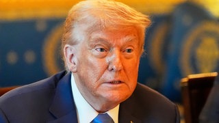 US-Präsident Donald Trump sitzt an einem Konferenztisch im Weißen Haus und blickt erstaunt.