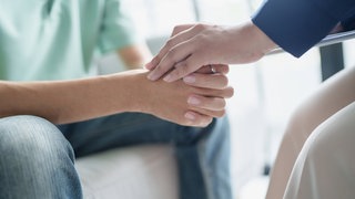 Ein trauriger Mann sitzt auf einem Sofa und bespricht psychische Probleme mit einer Psychologin, die seine Hände hält.