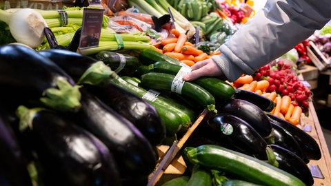 Ein Mann steht in einem Supermarkt an einer Auslage in der Obst und Gemüseabteilung.