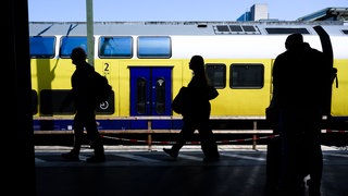 Die Silhouetten von Fahrgästen zeichnen sich am Hauptbahnhof Hannover vor einem Regionalzug ab.