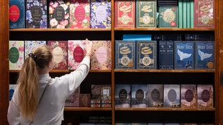 Eine junge Frau nimmt ein Buch einer Buch-Reihe aus einem Regal an einem Messestand auf der Frankfurter Buchmesse.