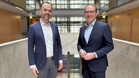 Korrespondent Oliver Neuroth und Bundesinnenminister Alexander Dobrindt stehen in der Halle im ARD-Hauptstadtstudio nebeneinander und schauen in die Kamera