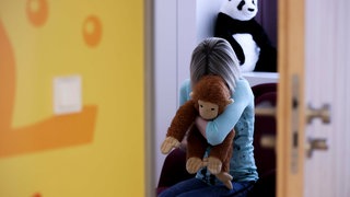 Ein Mädchen sitzt in einem Raum und vergräbt ihr Gesicht in einem Kuscheltier (Symbolbild)