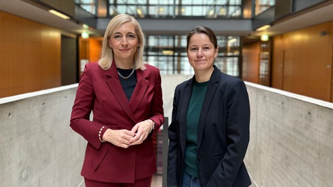 Gesundheitsministerin Nina Warken und Korrespondentin Birthe Sönnichsen stehen in der Halle im ARD-Hauptstadtstudio nebeneinander und schauen in die Kamera
