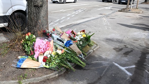 Blumen liegen an einer Unfallstelle in Ludwigsburg nach einem mutmaßlichen Autorennen mit zwei Toten. Davor sind Kreidezeichen und Unfallspuren auf dem Pflaster zu sehen.