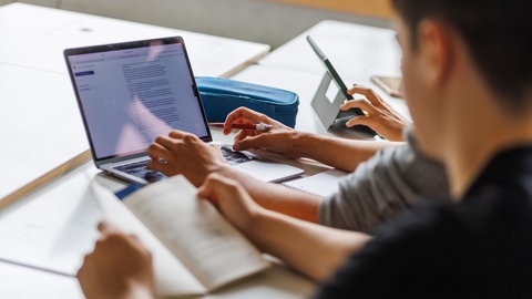 Schüler eines Gymnasiums sitzen vor einem Computer und benutzen ein KI-Tool.