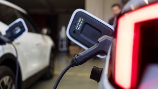 Ein Ladestecker steckt in einem Auto in einer Halle von der Firma Ambibox. Die Firma baut bidirektionale Ladesysteme.