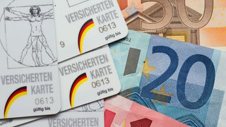 Krankenkassen-Karten für Pflichtversicherte liegen neben Euro-Scheinen.