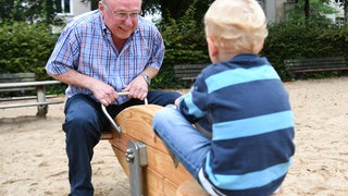 Ein "Leih-Opa" wippt mit einem dreijährigen Jungen auf dem Spielplatz.