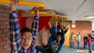 Schülerinnen und Schüler hangeln sich an einer Decken-Konstruktion durch einen Gang in ihrer Schule, um mehr Bewegung im Alltag zu haben.