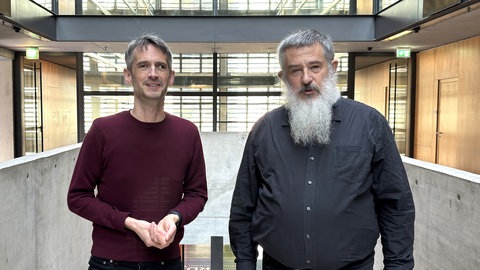 Korrespondent Markus Sambale und Stephan Kramer stehen in der Eingangs-Halle im ARD-Hauptstadtstudio nebeneinander und schauen in die Kamera