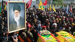 Menschen halten ein Foto des verstorbenen iranischen Obersten Führers, Ayatollah Ali Chamenei, während sie der Beerdigung von Kämpfern der Kata'ib Hisbollah beiwohnen, die bei einem US-Luftangriff in der Provinz Babil südwestlich von Bagdad getötet wurden