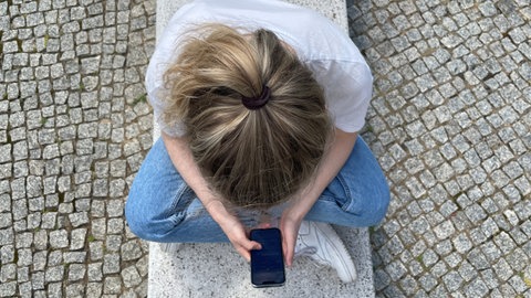 Typische Haltung in heutiger Zeit: mit gesenktem Kopf auf das Handy schauen