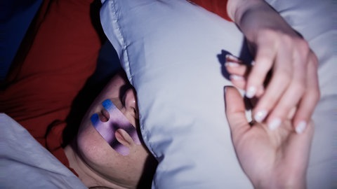Eine Frau liegt mit einem Mundpflaster im Bett.