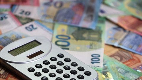 Nach der Landtagswahl in RLP forder Kommunen von Gordon Schnieder mehr Geld. Ein Taschenrechner liegt auf verschiedenen Euro-Banknoten.