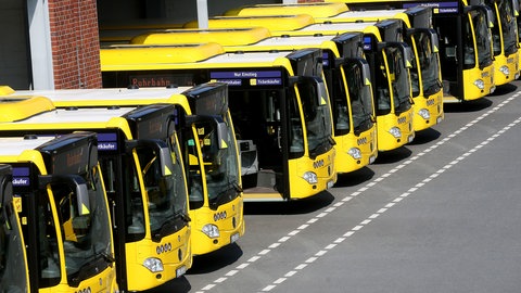 Eine ganze Reihe gelber Busse stehen in den Toreinfahrten eines Bus-Depots aus Backstein.