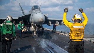 Ein Soldat der US-Marine gibt einer FA-18E Super Hornet das Signal zum Start vom Flugdeck des Flugzeugträgers USS Abraham Lincoln der Nimitz-Klasse während der Operation Epic Fury.