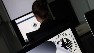 Eine Geheimdienst-Mitarbeiterin sitzt in der Zentrale des Bundesnachrichtendienstes (BND) in einem Schulungsraum vor einem Bildschirm mit dem Logo des BND.