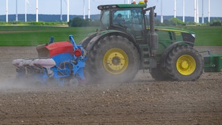 Ein Traktor pflügt einen Acker, im Hintergrund sind Windräder zu sehen