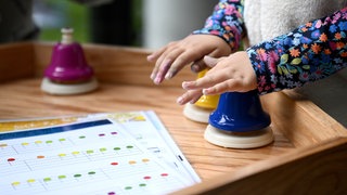 Ein Kind spielt mit bunten Glocken. Auf dem Tisch liegt ein farbiges Notenblatt.