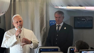 Papst Leo XIV. (l) spricht neben Vatikan-Sprecher Matteo Bruni zu Journalisten an Bord seines Fluges zum Houari Boumédiène International Airport in Algier