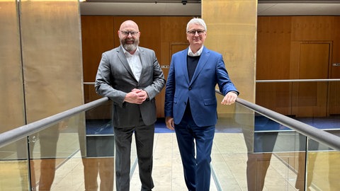 Dietrich Karl Mäurer und Sönke Rix stehen in der Halle im ARD-Hauptstadtstudio nebeneinander und schauen in die Kamera