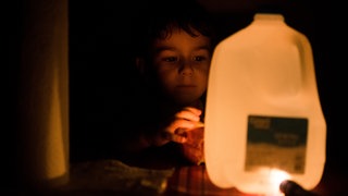 Resilienz nach Katastrophen: Ein Junge nutzt nach einem Stromausfall seine Taschenlampe, um damit einen Wasserkanister zu erleuchten.