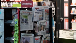 Tageszeitungen stecken vor einem Kiosk in Zeitungshaltern.
