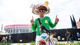 Ein mit Fanartikel bekleideter Mexiko-Fan steht vor dem Stadion.