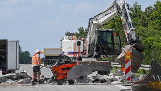 Ein Arbeiter sägt bei Hitze auf einer Autobahn die Fahrbahndecke auf.
