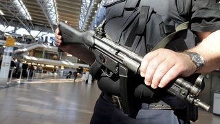 Ein mit einer Maschinenpistole bewaffneter und einer Schutzweste ausgestatteter Polizist patrouilliert am Flughafen