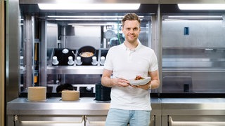 Dieses von Goodbytz zur Verfügung gestellte Foto zeigt Hendrik Susemihl, einer der Gründer des Hamburger Start-ups Goodbytz, vor einem Kochroboter. Er hält eine Schüssel mit Essen in der Hand und lächelt in die Kamera.