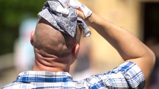 Hitze: Ein schwitzender Mann wischt sich am mit einem Stofftuch über den Kopf