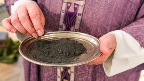 Ein Priester hält eine Schale mit Asche in der Hand. Für Katholiken gehört die Bemalung mit Aschekreuzen fest zum Aschermittwoch.