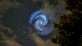 Weiß-bläulich schimmert eine Lichtspirale am Nachthimmel.