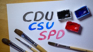 Parteinamen CDU, CSU und SPD mit Wasserfarben auf weißes Papier gemalt.